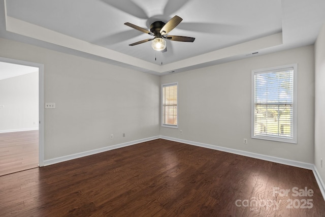 unfurnished room with visible vents, baseboards, a raised ceiling, dark wood-style flooring, and ceiling fan