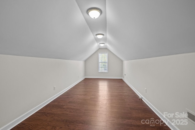additional living space with baseboards, visible vents, dark wood-style flooring, and vaulted ceiling