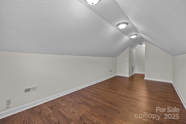additional living space featuring dark wood-type flooring, visible vents, baseboards, and vaulted ceiling