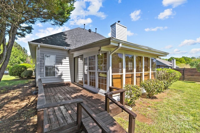 rear view of house with a wooden deck, a sunroom, fence, a chimney, and a shingled roof