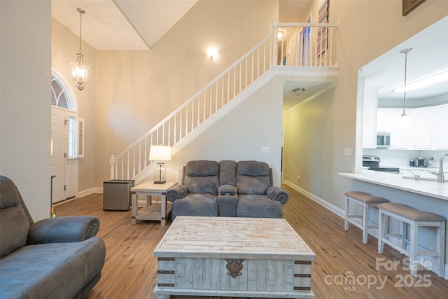 living room featuring high vaulted ceiling, baseboards, wood finished floors, and stairway