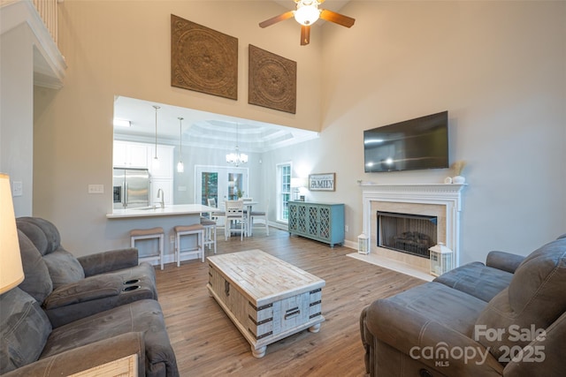living room with a fireplace, wood finished floors, a high ceiling, and ceiling fan with notable chandelier