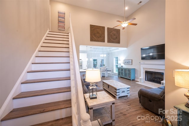 stairs with a high ceiling, wood finished floors, baseboards, a fireplace, and ceiling fan with notable chandelier