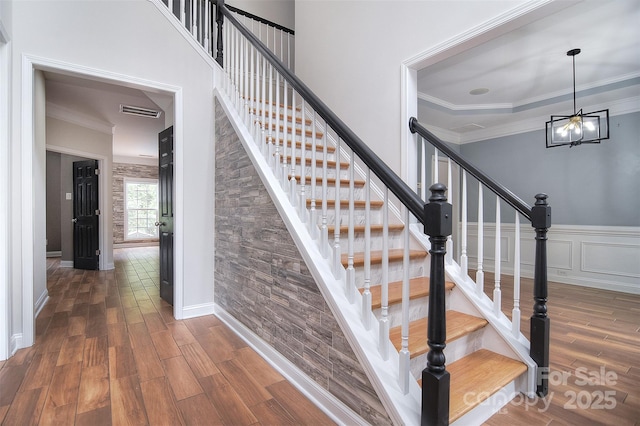 stairway with crown molding, a chandelier, wood finished floors, and visible vents