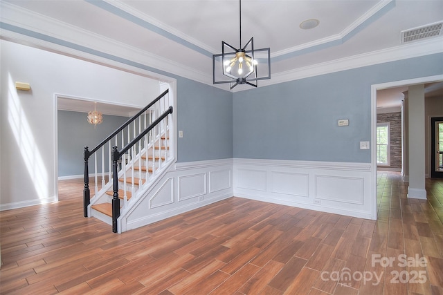 spare room with stairway, wood finished floors, a raised ceiling, and a notable chandelier