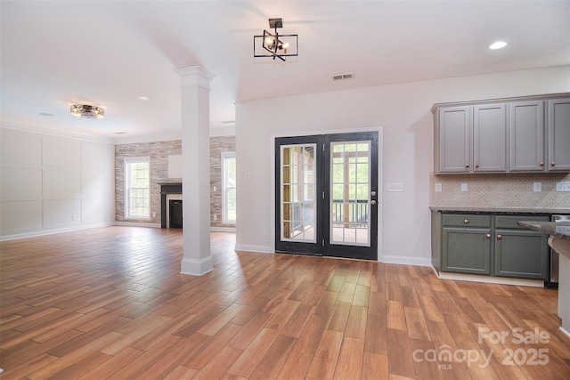 unfurnished living room featuring french doors, light wood finished floors, baseboards, visible vents, and ornate columns