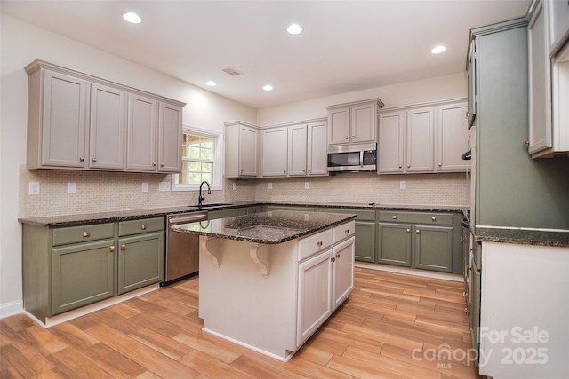 kitchen with light wood-type flooring, appliances with stainless steel finishes, a center island, and a sink