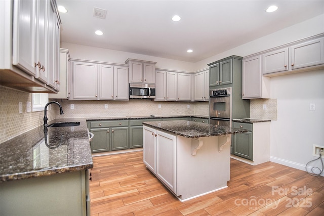 kitchen with dark stone counters, a sink, light wood-style flooring, appliances with stainless steel finishes, and visible vents