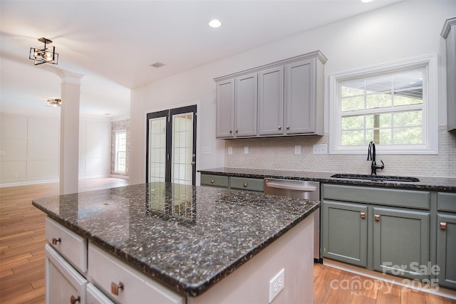 kitchen featuring dishwasher, ornate columns, gray cabinetry, and a sink