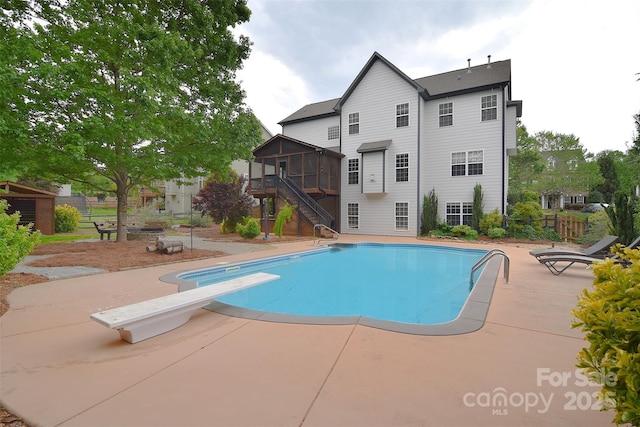 outdoor pool with stairs, fence, a diving board, a patio area, and a sunroom