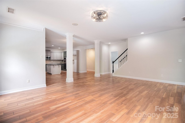 unfurnished living room featuring stairway, light wood finished floors, baseboards, visible vents, and decorative columns