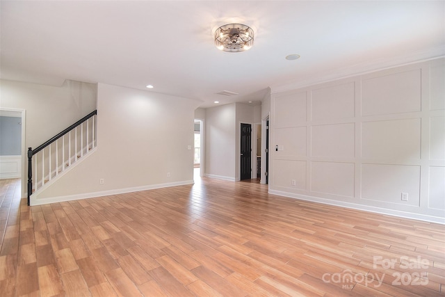 unfurnished living room featuring a decorative wall, light wood-style floors, and stairs