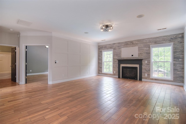 unfurnished living room featuring visible vents, crown molding, baseboards, a glass covered fireplace, and light wood-style flooring