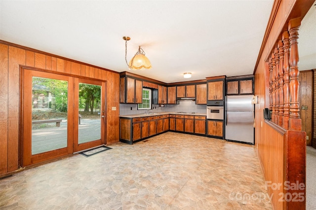 2415 Hargette Rd, Monroe, NC 28112 - kitchen with stone finish flooring, wooden walls, under cabinet range hood, brown cabinetry, and stainless steel appliances