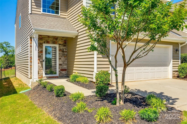 doorway to property with concrete driveway, roof with shingles, fence, and stone siding