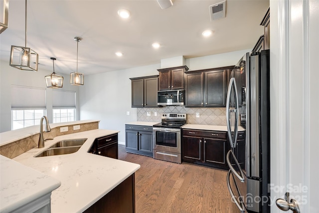 kitchen with wood finished floors, tasteful backsplash, a sink, decorative light fixtures, and stainless steel appliances