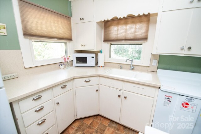 kitchen with light countertops, white microwave, a sink, and white cabinetry
