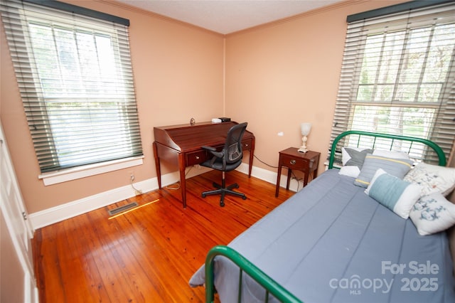 bedroom featuring crown molding, visible vents, baseboards, and hardwood / wood-style floors