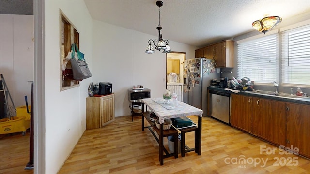 kitchen with a sink, dark countertops, light wood-style floors, and stainless steel appliances