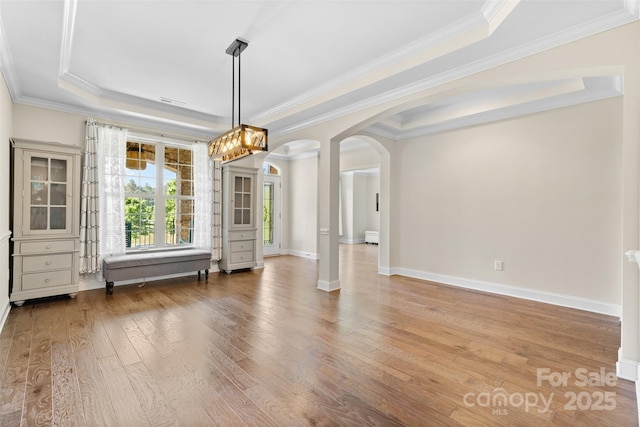 unfurnished dining area featuring arched walkways, hardwood / wood-style floors, a raised ceiling, crown molding, and baseboards