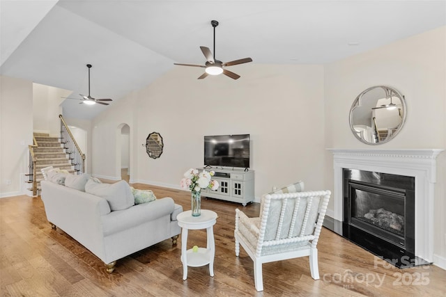 living area with ceiling fan, arched walkways, stairs, wood finished floors, and vaulted ceiling