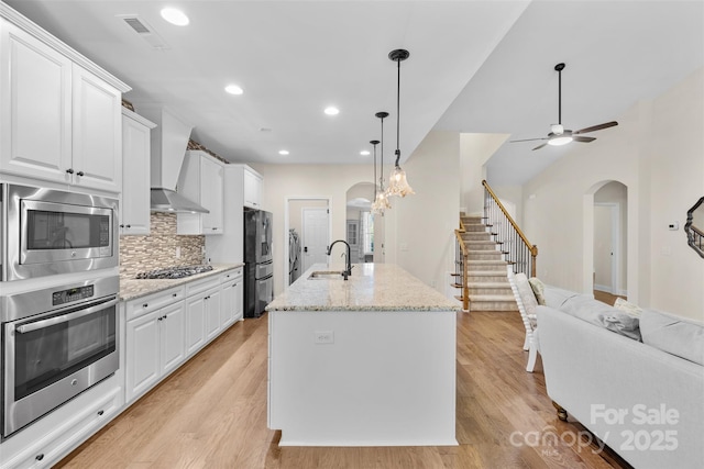 kitchen with appliances with stainless steel finishes, arched walkways, wall chimney exhaust hood, recessed lighting, and a sink