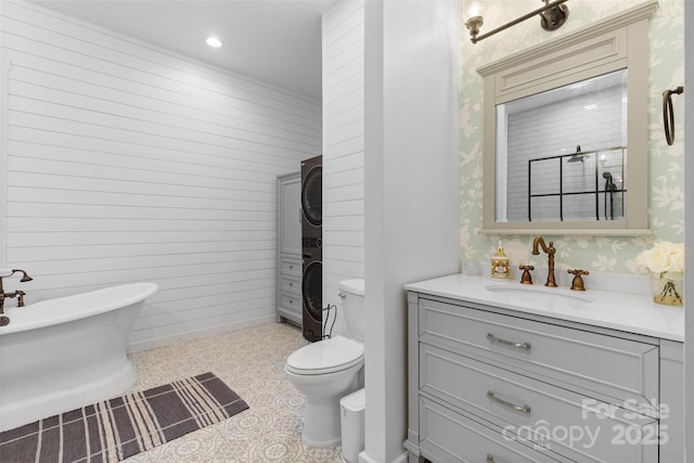 bathroom with stacked washer / dryer, a freestanding tub, toilet, vanity, and wallpapered walls