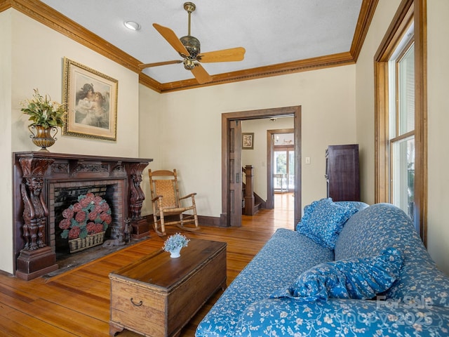 living area featuring baseboards, a brick fireplace, ceiling fan, crown molding, and wood finished floors