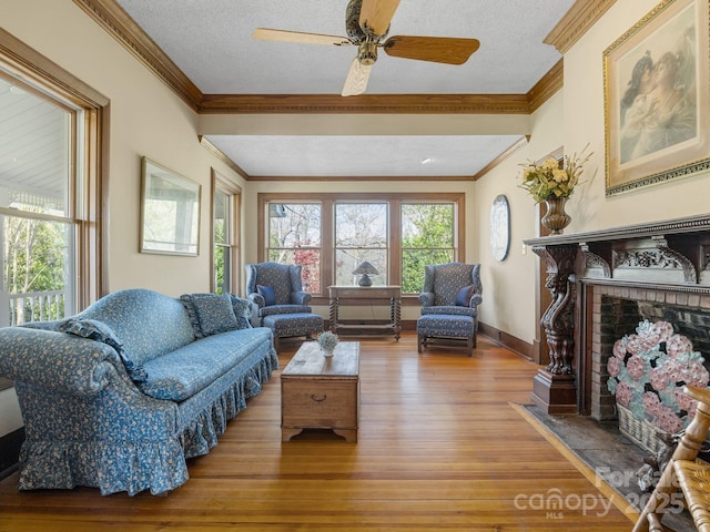 living area featuring a fireplace, a textured ceiling, crown molding, a ceiling fan, and wood finished floors