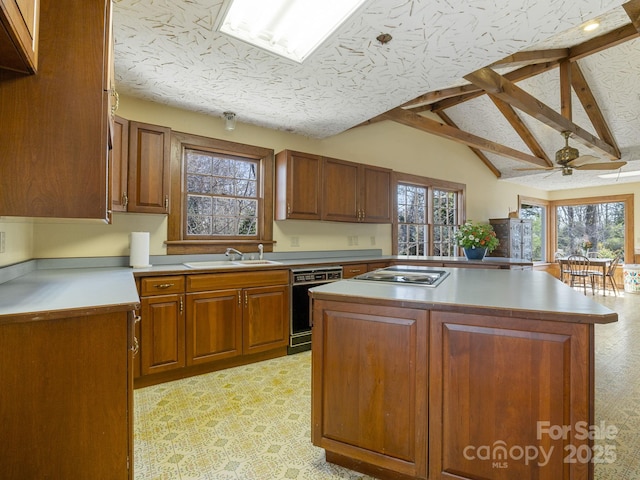 kitchen with stainless steel stovetop, a textured ceiling, dishwasher, a sink, and vaulted ceiling with beams