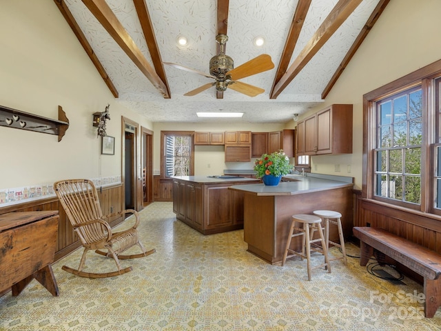 kitchen with lofted ceiling with beams, a peninsula, a textured ceiling, wood walls, and wainscoting