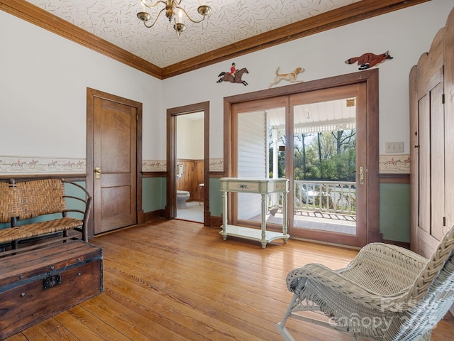 interior space with ornamental molding, a wainscoted wall, a notable chandelier, and light wood-style floors