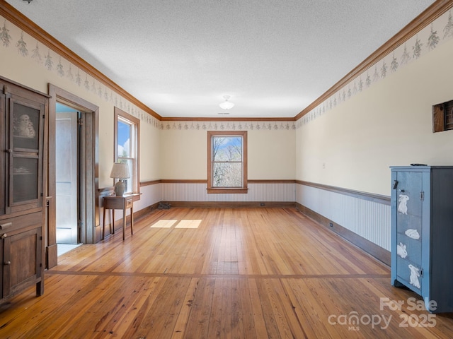 spare room with wainscoting, a textured ceiling, and light wood-style flooring