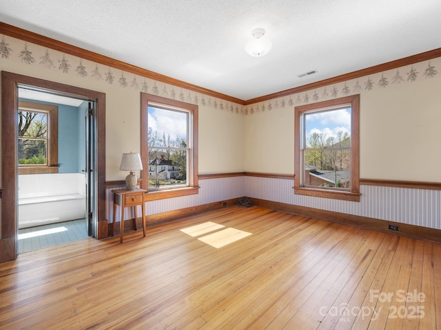 spare room with light wood-style flooring, a healthy amount of sunlight, wainscoting, and visible vents