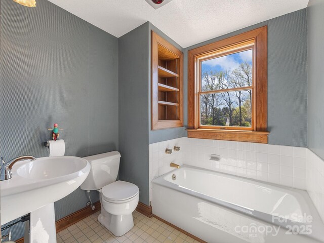 full bath with a sink, toilet, a bath, and a textured ceiling