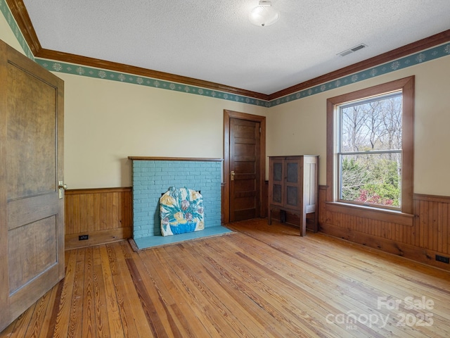 unfurnished living room with visible vents, a textured ceiling, wooden walls, wainscoting, and wood-type flooring