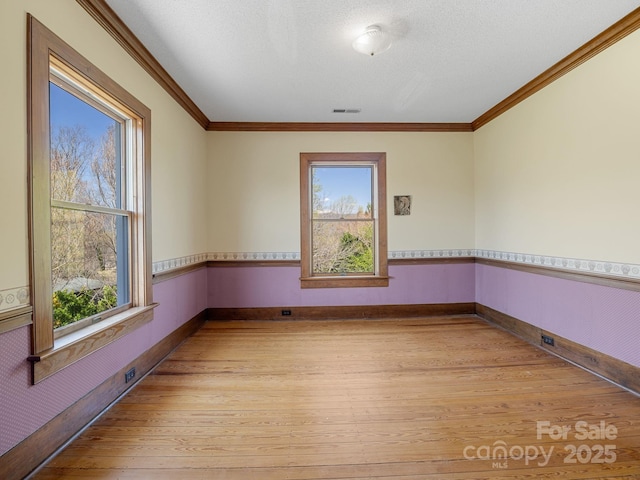 spare room with light wood-style floors, crown molding, a textured ceiling, visible vents, and baseboards