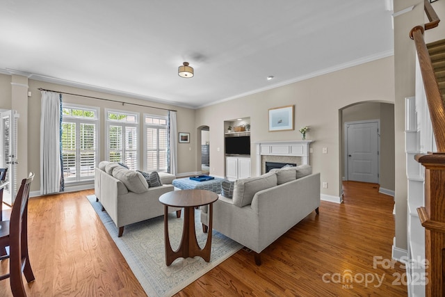 living area with baseboards, arched walkways, ornamental molding, a fireplace, and wood finished floors