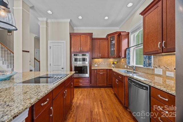 kitchen with glass insert cabinets, appliances with stainless steel finishes, light stone counters, a sink, and light wood finished floors