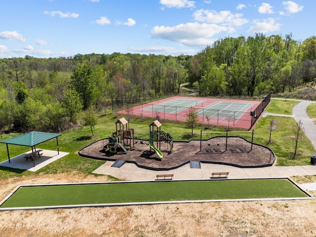 surrounding community featuring a tennis court, a forest view, and playground community