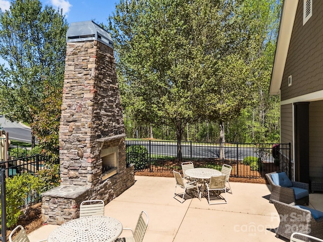 view of patio with outdoor dining space, fence, and an outdoor stone fireplace