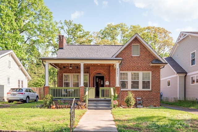 view of front facade featuring a porch, roof with shingles, a front lawn, brick siding, and a chimney