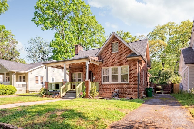 bungalow-style home featuring a chimney, driveway, a front lawn, brick siding, and a shingled roof
