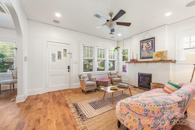 living room featuring wood-type flooring, a wealth of natural light, a ceiling fan, and a brick fireplace