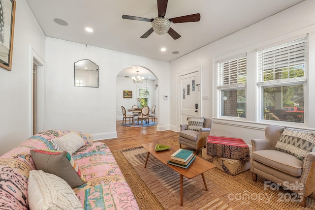 living room with baseboards, arched walkways, recessed lighting, ceiling fan with notable chandelier, and light wood-style flooring