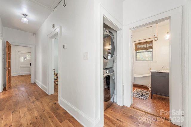laundry area with baseboards, light wood-type flooring, stacked washer / drying machine, and laundry area