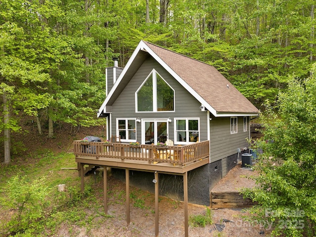 rear view of property featuring a wooden deck, crawl space, a view of trees, a chimney, and cooling unit