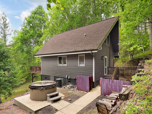 back of property featuring a hot tub, a shingled roof, central air condition unit, and a wooden deck