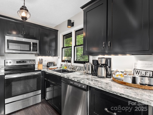 kitchen featuring light stone countertops, dark wood-style floors, dark cabinetry, a sink, and stainless steel appliances