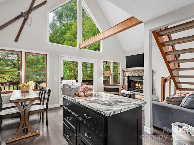 kitchen with beam ceiling, a stone fireplace, open floor plan, high vaulted ceiling, and dark cabinetry